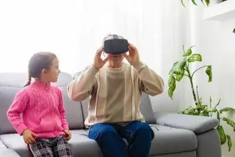 Възрастен мъж, носещ очила за виртуална реалност у дома с внучка до него