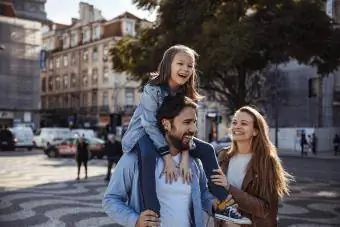 Baba ve kızı omuzlarında gülümsüyor ve anne de yanlarında