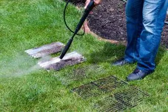 Homem lavando placas sujas de churrasqueira usando um poderoso jato de água de uma mangueira de pressão