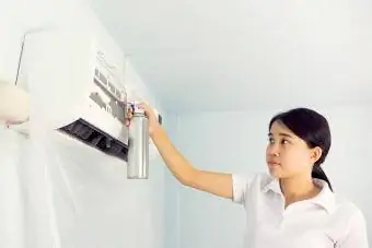 Mujer limpiando el aire acondicionado con un agente limpiador de espuma