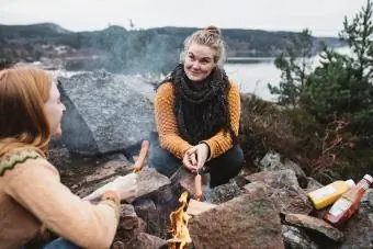 Gratë që përgatisin hotdogs mbi zjarr kampi