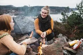 Kvinner tilbereder pølser over bål