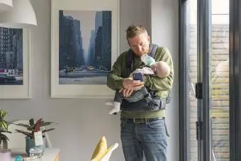 tata gleda u telefon dok drži bebu