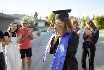 Giovane donna vestita con un cappello da laurea circondata dai suoi amici e dalla sua famiglia