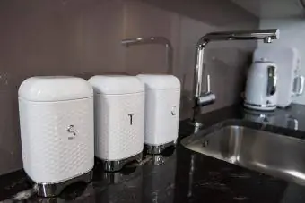 Botes cuadrados blancos de té, azúcar y café sobre una encimera de cocina