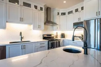 Cozinha moderna com armários brancos, ilha escura e detalhes dourados