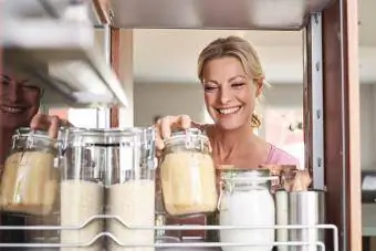 Usmievavá žena v kuchyni berie nádobu z kuchynskej skrinky