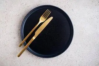 Празна черна керамична чиния и златни вилица и нож