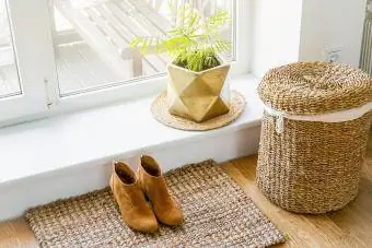 Lantai kayu keras dengan keset goni, pot bunga, dan keranjang cucian di dekat jendela