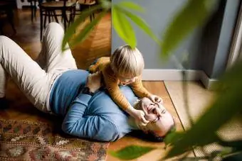 Παιχνιδιάρικη κόρη που τσιμπά τα μάγουλα του χαρούμενου πατέρα στο πάτωμα στο σπίτι