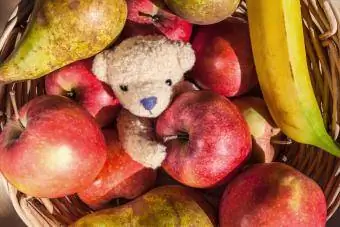 Χαριτωμένο μικρό αρκουδάκι μέσα σε καλάθι με φρούτα με μήλα, αχλάδια και μπανάνα