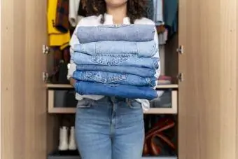 Kobieta stojąca przed szafą, trzymająca stos niebieskich dżinsów