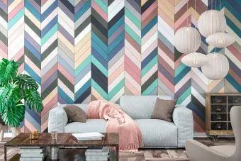Soggiorno moderno con divano grigio, sedia, tavolo e decorazioni su pavimento in legno davanti a una parete piastrellata con motivo a spina di pesce multicolore