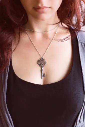 Mulher com cabelo ruivo escuro usando um colar de chave vintage