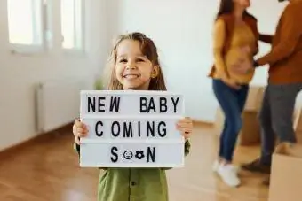 Fröhliches kleines Mädchen hält eine Ankündigungsnachricht mit einem Text in der Hand, dass bald ein neues Baby kommt