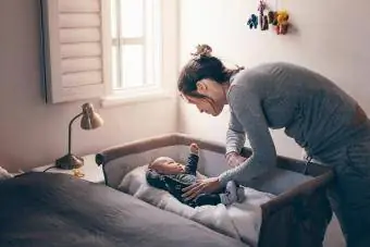 Mladá matka sa pozerá na svoje dieťa spí v postieľke