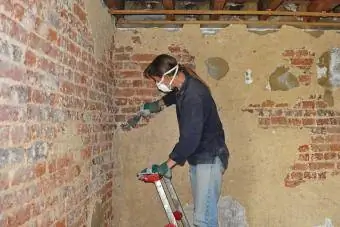 DIY, γυναίκα που καθαρίζει τον τοίχο από τούβλα ενός δωματίου