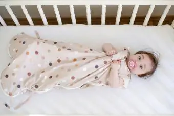 Baby im Schlafsack liegt in einem Kinderbett