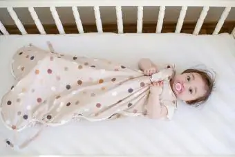 Bebê em saco de dormir deitado em um berço