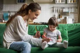 Lächelnder Babysitter und Kind zeichnen, während sie zusammen auf dem Sofa sitzen