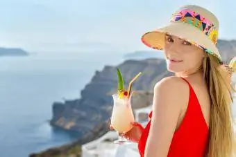 Wanita memegang koktail pina colada dan menikmati pemandangan