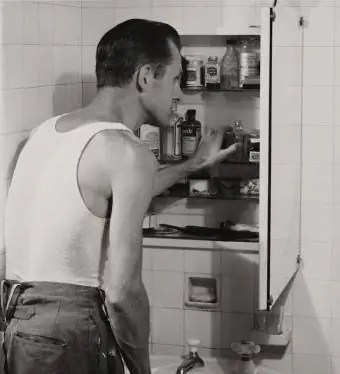Mies katselee kylpyhuoneessa olevaa lääkekaappiaan, noin 1955