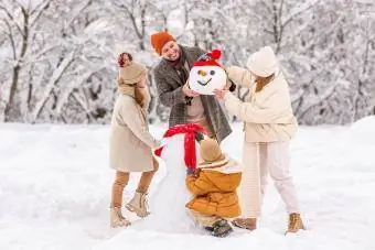 Glückliche Kinder formen im Winter gemeinsam mit den Eltern einen lustigen Schneemann