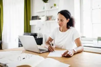 Mulher olhando para o computador e fazendo anotações