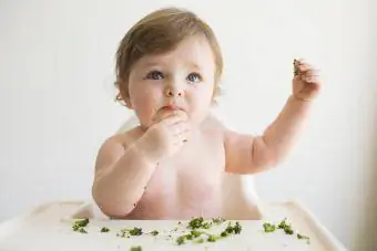 Бебе момче, което яде броколи в столче за хранене
