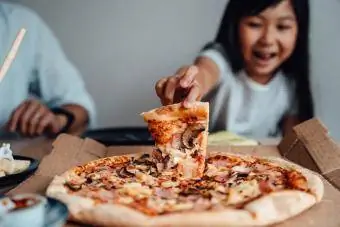Fröhliches junges Mädchen hält ein Stück Pizza