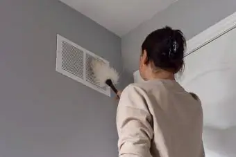 Mujer limpiando la salida de aire de retorno con plumero