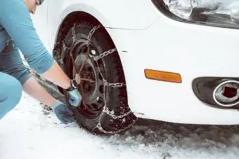 En kvinne monterer snødekkkjeder på en bil