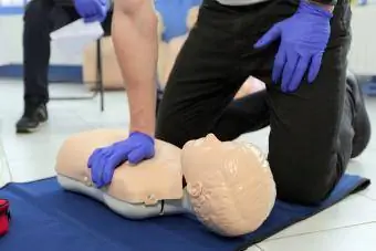 Мъж, демонстриращ CPR върху тийнейджърски манекен в час по първа помощ