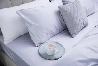 Yumuşak ipeksi yatak örtüleri ile yatakta bir fincan kahve
