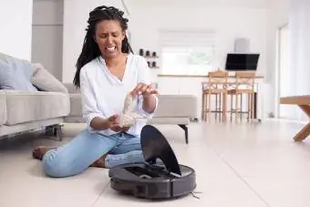 Mujer que parece disgustada mostrando el filtro obstruido y la caja de polvo llena del robot aspirador