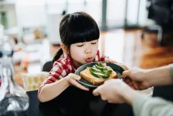 دختر کوچک آسیایی دوست داشتنی که پشت میز آشپزخانه نشسته است