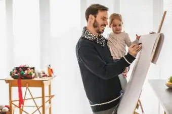 Menina se divertindo enquanto desenha em um quadro com o pai