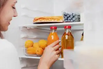 Mano della donna che prende la bottiglia di vetro del succo dal frigorifero aperto