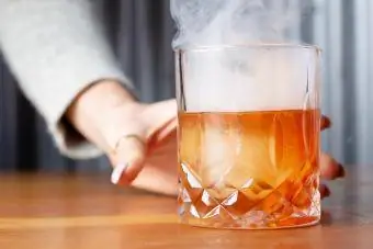 Hand som håller rökt cocktail på bordet