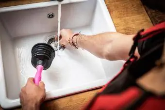 Tukang paip menggunakan pelocok paip untuk membaiki sinki dapur