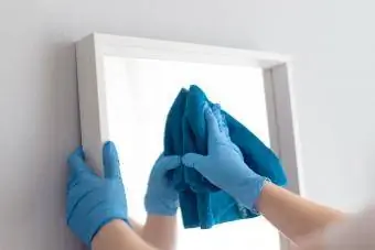 Frau putzt Spiegel mit Lappen