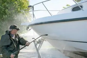 Човек, който използва машина за почистване под налягане, за да почисти корпуса на лодката