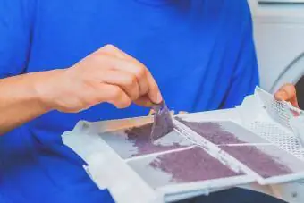 muž odstraňuje vlákna z prachového filtra bubnovej sušičky