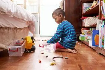 ילד צעיר יושב על הרצפה מרים את הצעצועים שלו