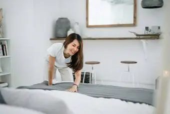 Frau macht ihr Bett und räumt ihr Schlafzimmer auf