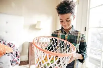 Batang lalaki na may dalang basket para sa mga laruan na naglilinis ng kanyang silid