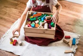 პატარა გოგონა ასუფთავებს სათამაშოების ყუთს სახლში