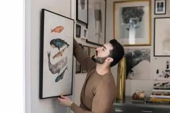 Lelaki muda menggantung lukisan di dinding di rumah