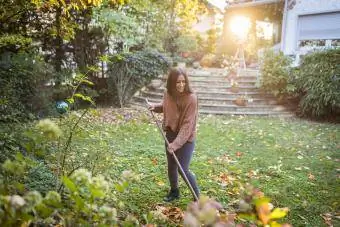 Dona feliç escombrant el jardí amb escombra al pati del darrere
