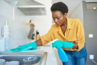 אישה צעירה מנקה דלפק במטבח בבית